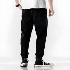 Black ribbed velvet trousers with tapered legs, elastic cuffs, and drawstring waist