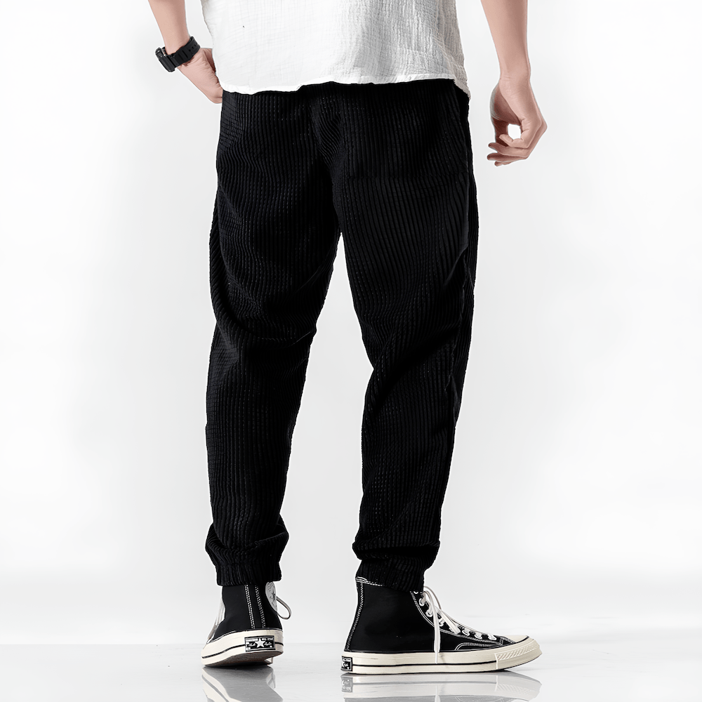 Black ribbed velvet trousers with tapered legs, elastic cuffs, and drawstring waist
