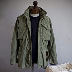 Green heritage jacket on mannequin with hood, drawstring waist, and flap pockets