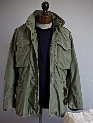 Green heritage jacket on mannequin with hood, drawstring waist, and flap pockets