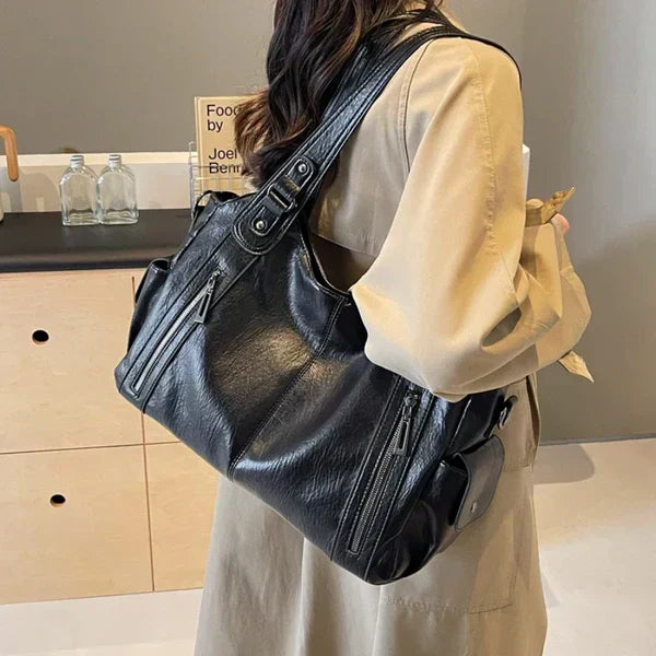 Black leather handbag slung crossbody with front zips and dual handle straps