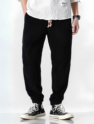 Black ribbed velvet trousers with tapered fit, elastic cuffs, and drawstring waist