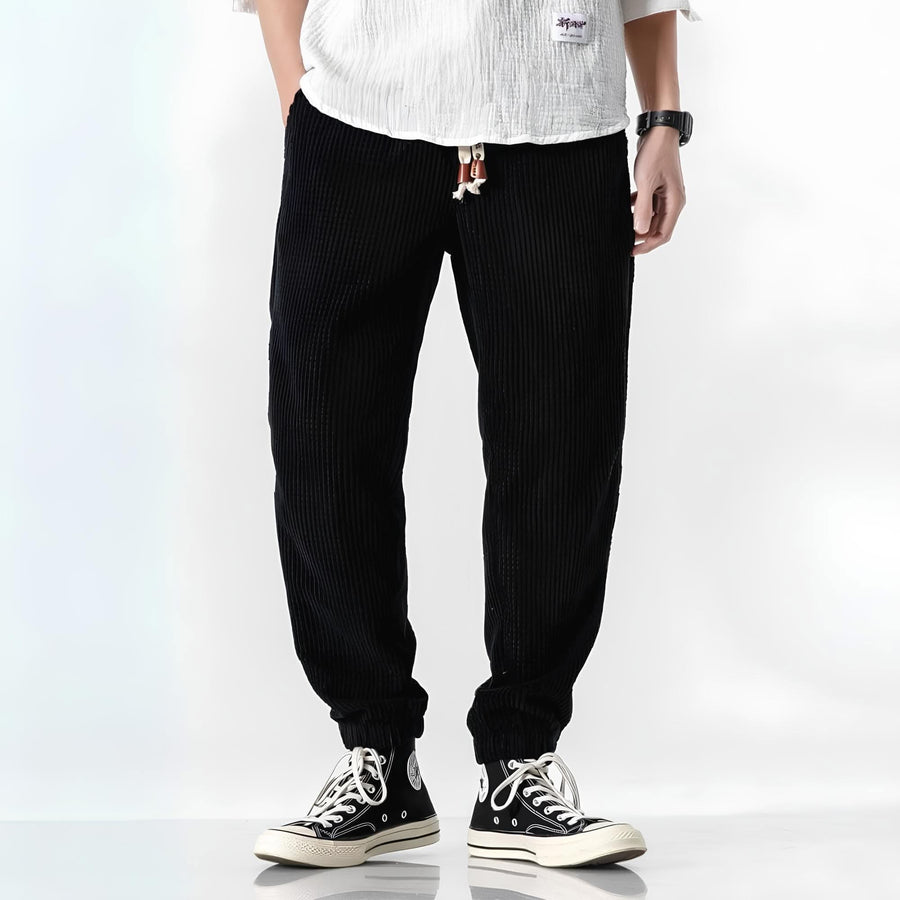 Black ribbed velvet trousers with tapered fit, elastic cuffs, and drawstring waist