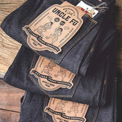 Indigo denim jeans with patch labels and contrast orange stitching on folded pair