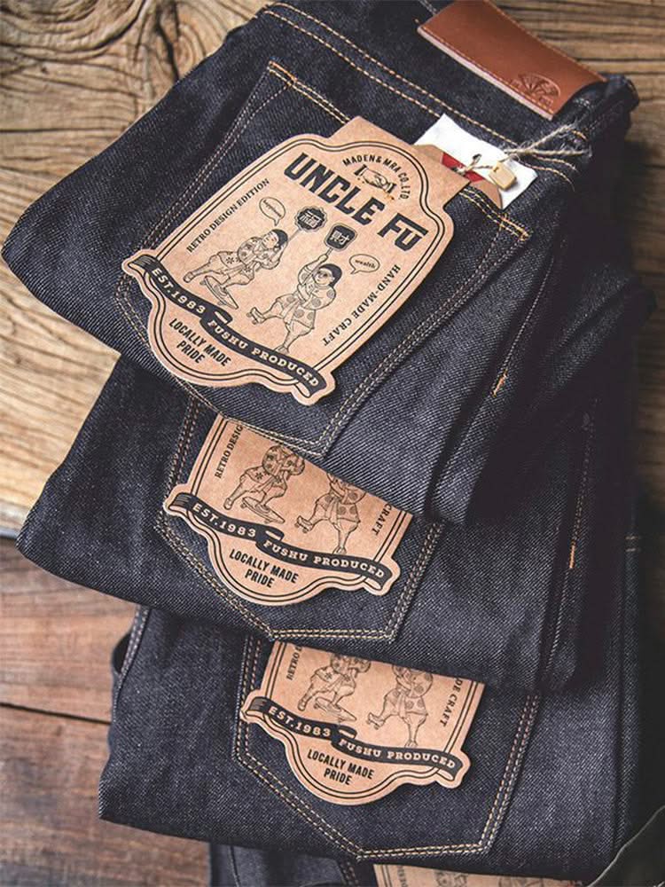 Indigo denim jeans with patch labels and contrast orange stitching on folded pair
