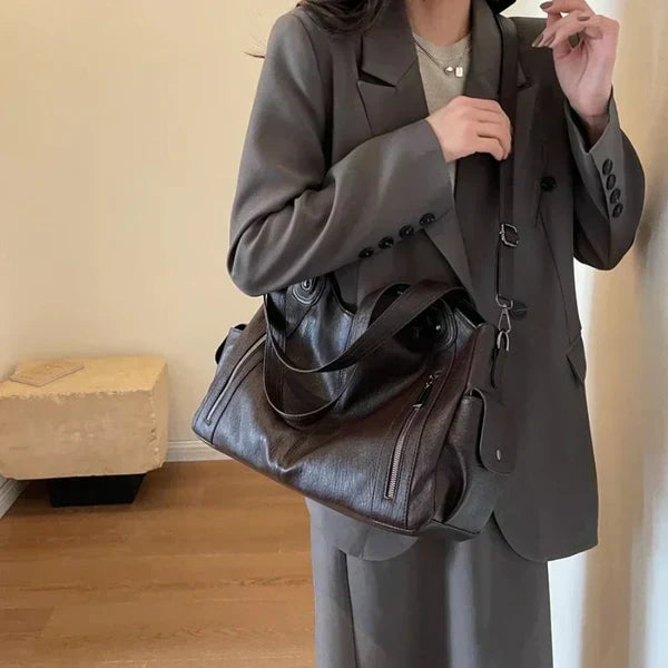 Black leather handbag with dual top handles, long strap, and front zip compartments