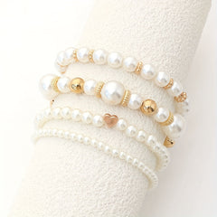 Pearl heart bracelet set display on light fabric with white pearls and gold heart charms