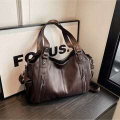 Coffee-brown leather handbag with top handles, side zippers, and adjustable shoulder strap