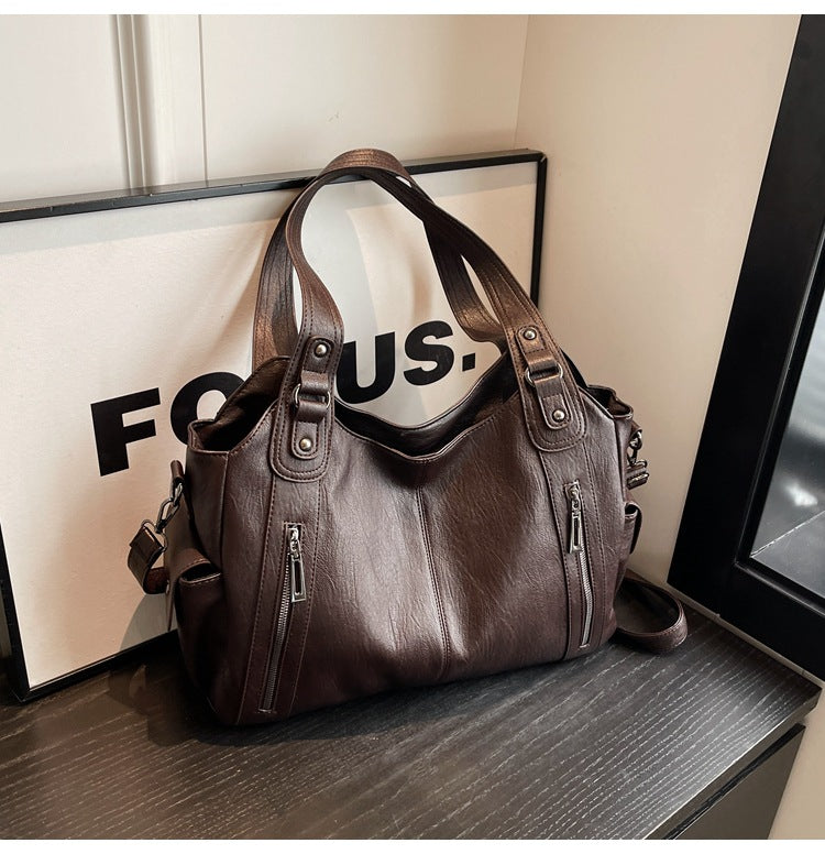 Coffee-brown leather handbag with top handles, side zippers, and adjustable shoulder strap