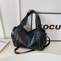 Black leather handbag with dual top handles, side zippers, and crossbody strap