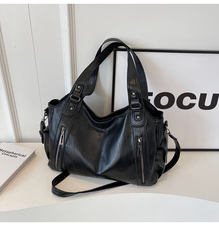 Black leather handbag with dual top handles, side zippers, and crossbody strap