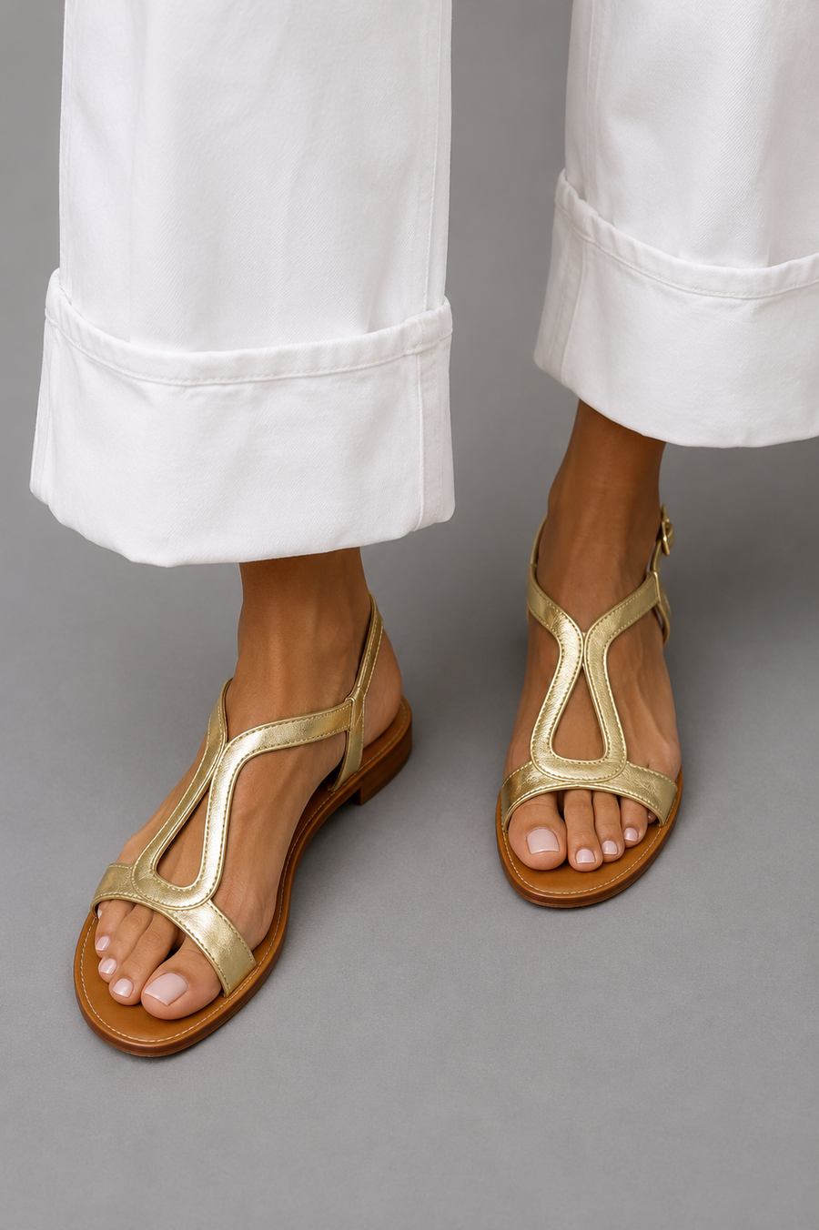 Gold thong sandals with open toe, curved straps, and low flat tan sole