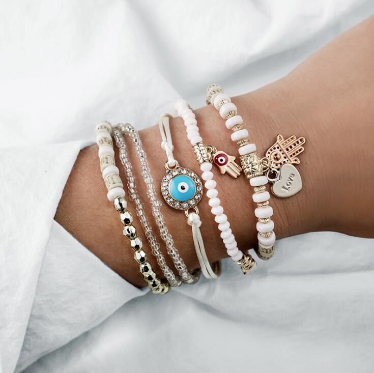 Beaded love bracelet set with charms, including evil-eye and heart tags on wrist