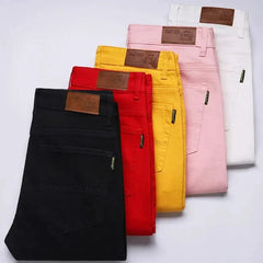 Assorted colored denim jeans folded together, including black, red, yellow, and pink