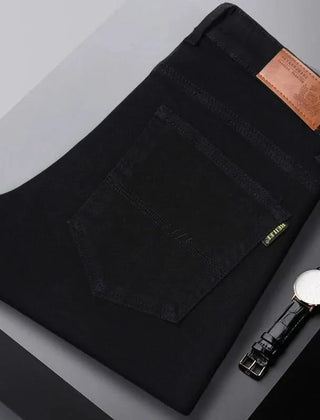 Black denim jeans folded flat, visible front pocket and brown leather logo patch