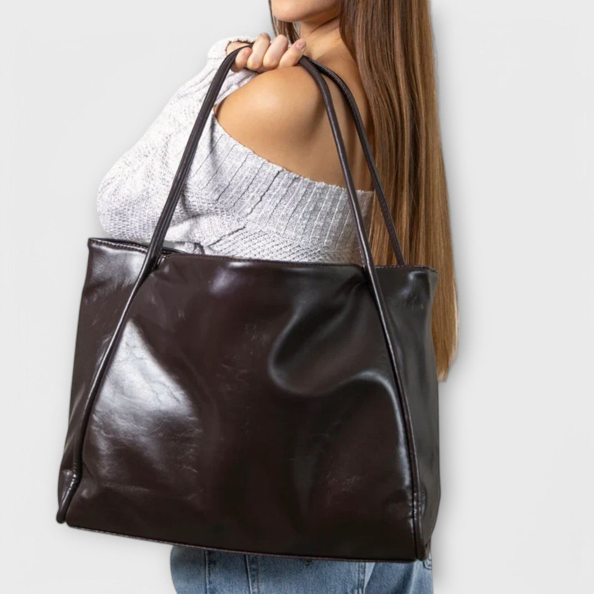 Dark brown leather-look tote bag held in front, wide handles and smooth front