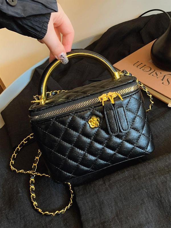 Black quilted crossbody bag with gold-tone chain, top zip, and decorative flower charm