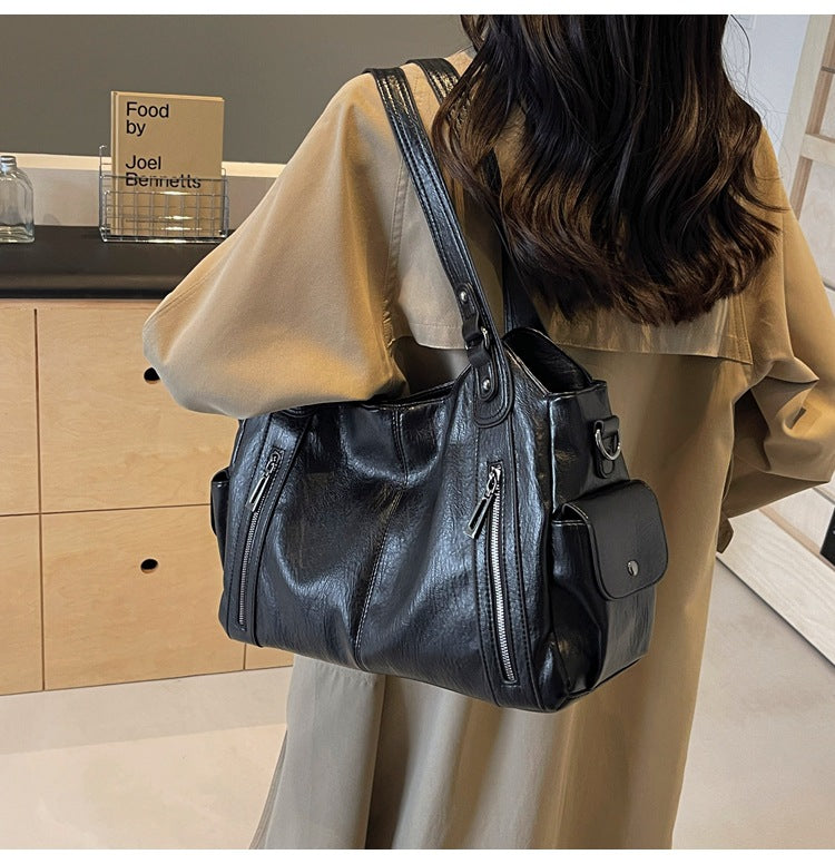 Black leather shoulder handbag with dual handles, front zip pockets, and attached strap