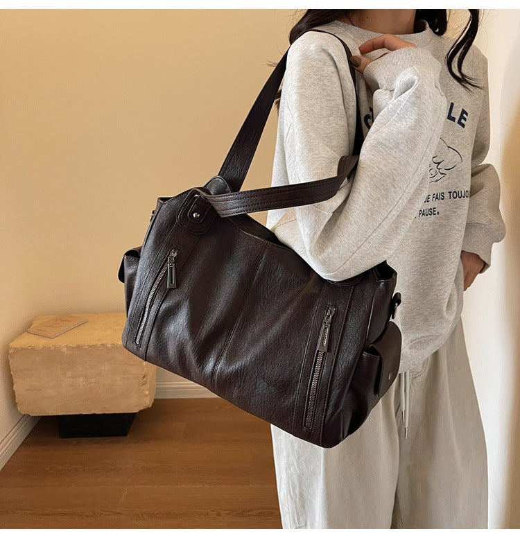 Dark brown leather handbag worn on shoulder with dual handles and zip front pockets