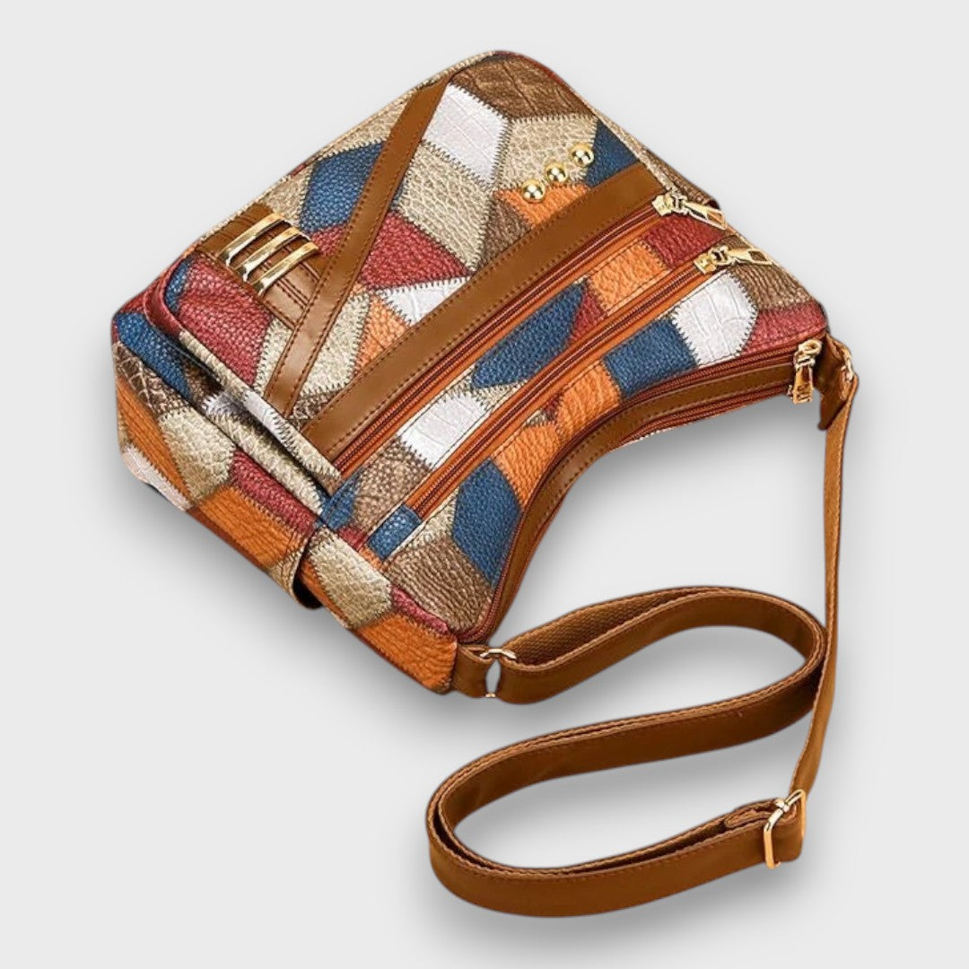 Patchwork leather shoulder bag with top zip closure, front detail tabs, and crossbody strap