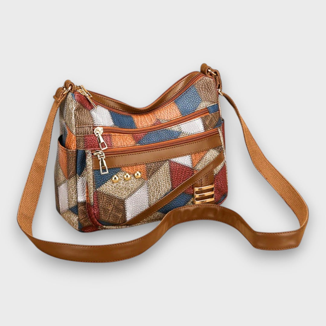 Patchwork leather crossbody bag with front zip pocket, gold accents, and long strap