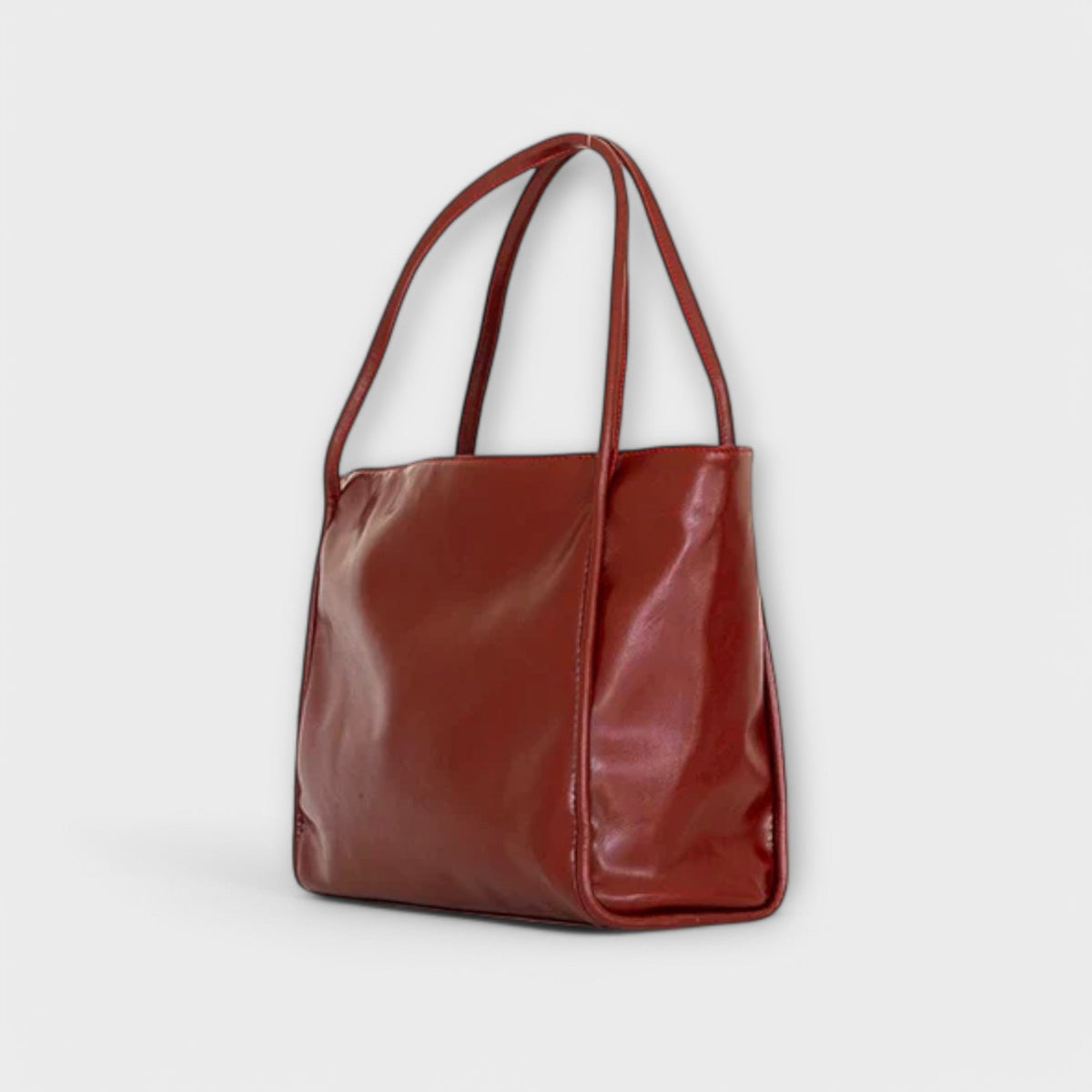 Red leather-look tote bag with wide handles, side view and glossy finish