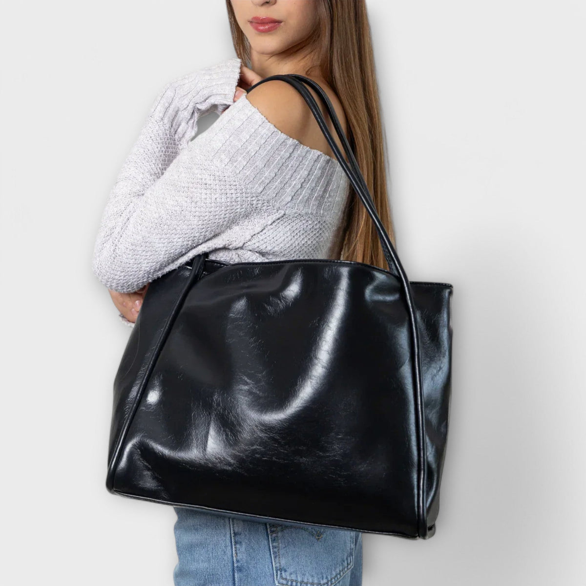 Black leather-look tote bag held over the shoulder, open top with wide handles