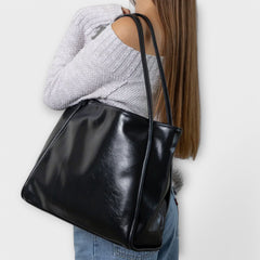 Black leather-look tote bag on shoulder, side view with wide top handles