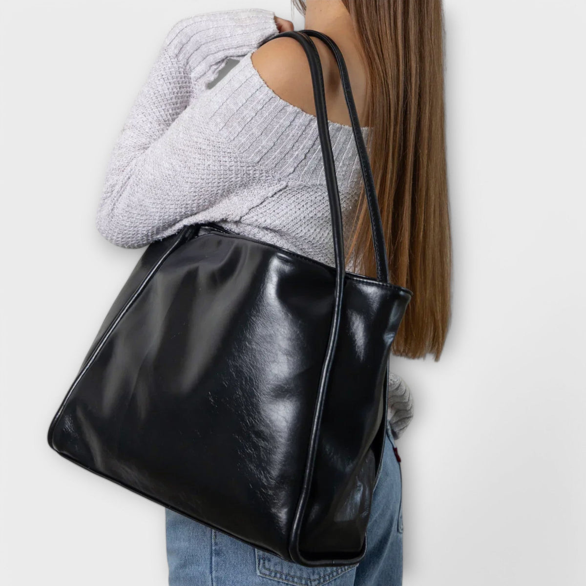 Black leather-look tote bag on shoulder, side view with wide top handles