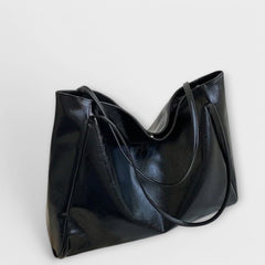 Dark glossy leather-look tote bag with curved top opening and wide handles